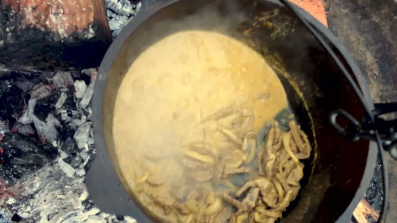 Man shows curried beef and rice dish simmering whilst camping in a camp oven cooker