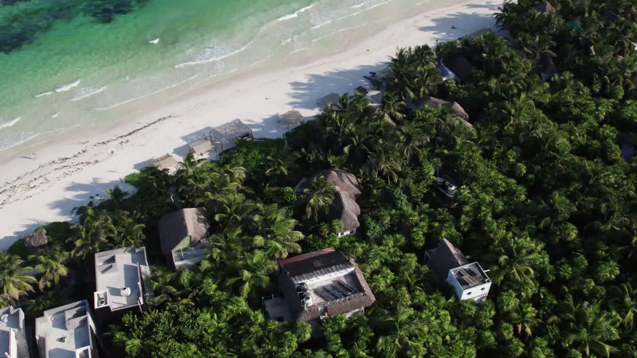 Aerial Orbit top down shot of huts and cabins surrounded by jungle and palm trees in front of a white sandy beach with crystal clear water in Tulum Mexico