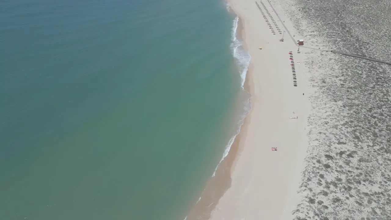 aerial view of a sandy yellow beach with umbrellas along the shore