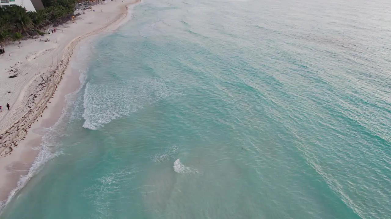 Aerial shot of crystal clear blue water with waves rolling into a white sand beach in Cancun Mexico