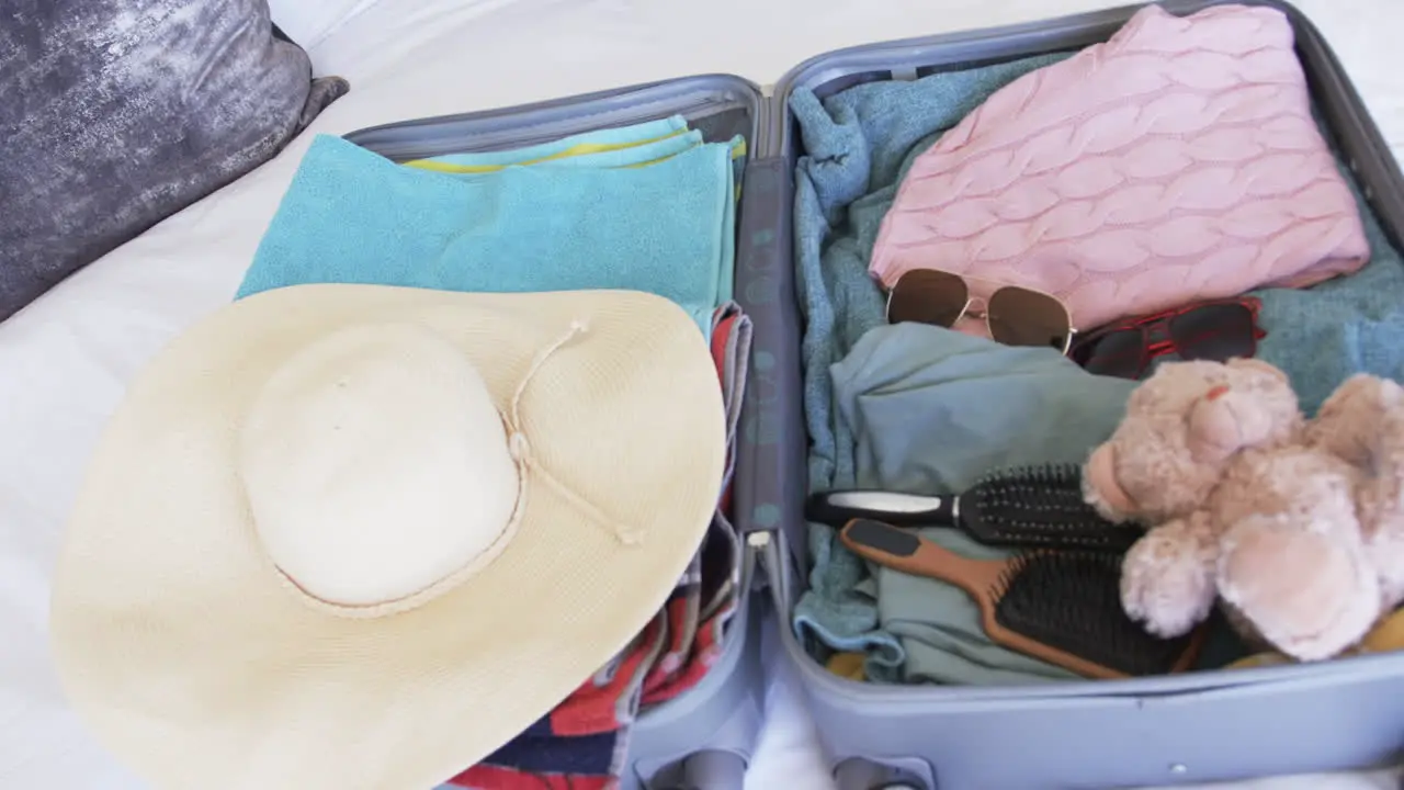 A suitcase is open revealing neatly packed clothes and a teddy bear