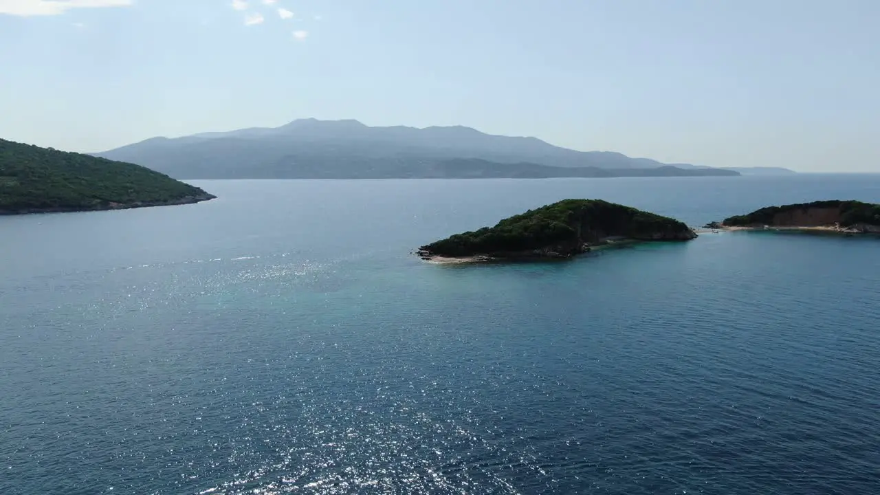 Drone view in Albania flying over the mediterranean ocean showing small islands and bigger Corfu island in the horizon sunny day in Ksamil