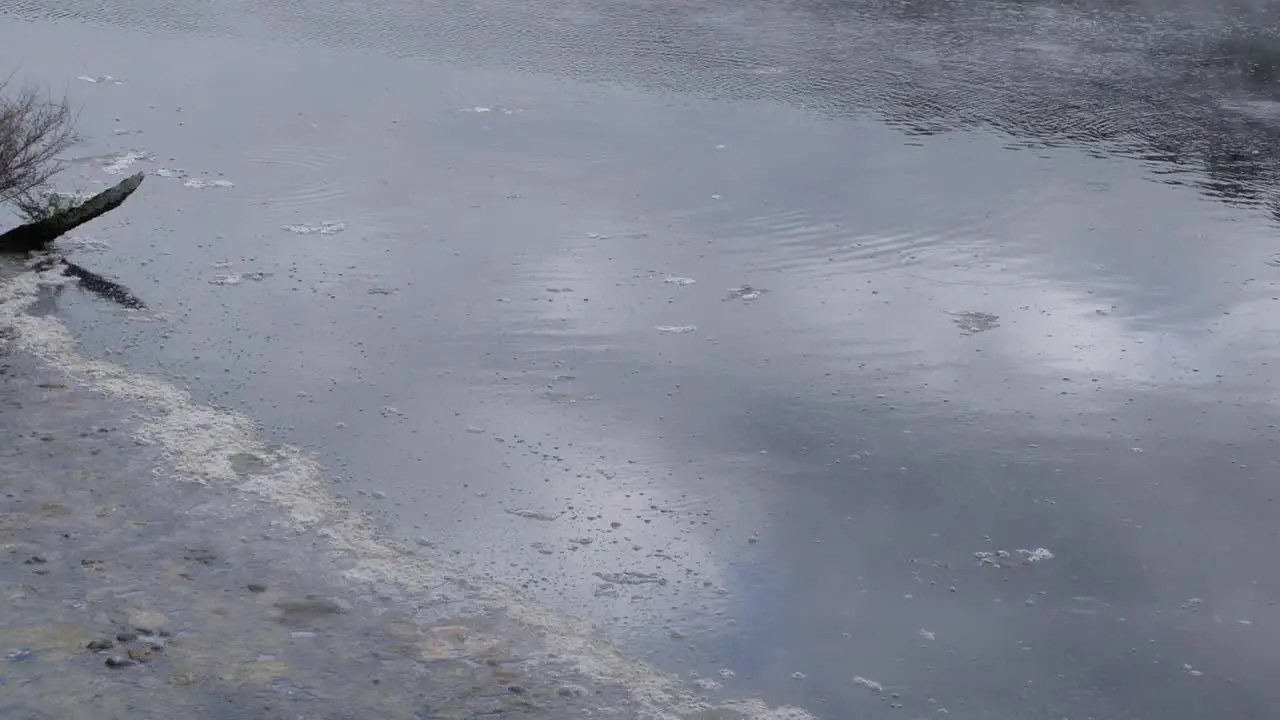 Close up of surface of water in sulphuric hot spring lake with atmospheric clouds of misty steam