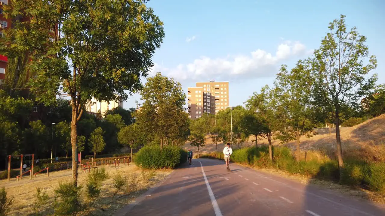 Two cyclists and a man riding an electric scooter driving on a bike path in the morning