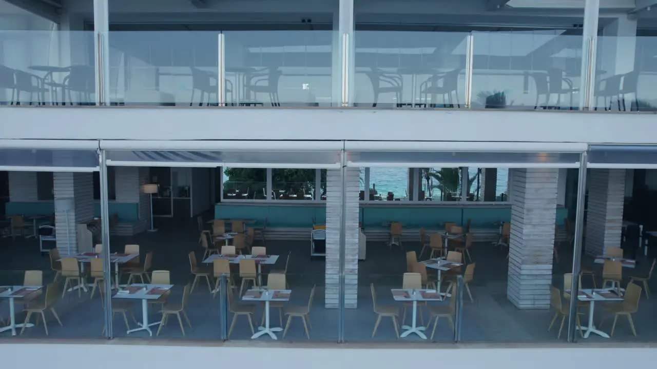 Aerial footage gliding along the balcony of a tourist resort building featuring a glass fence along with chairs and tables