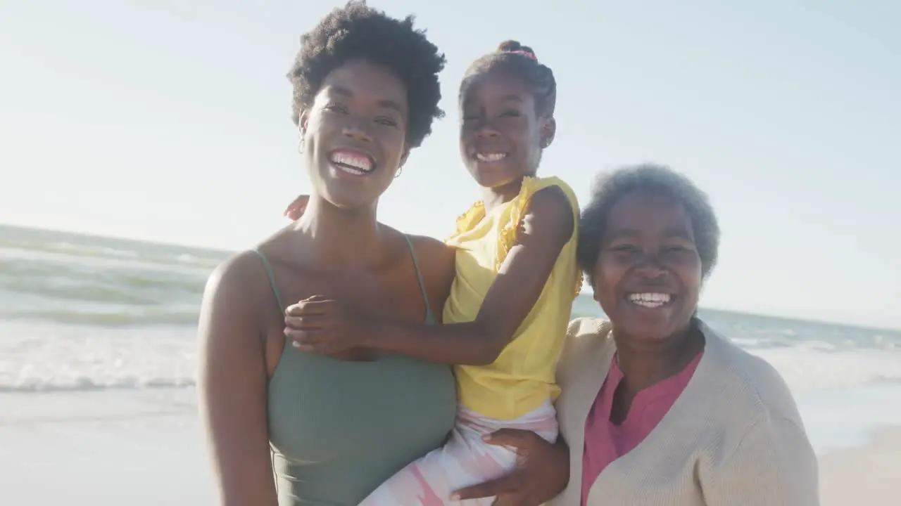 Portrait of happy african american grandmother mother and daughter smiling at beach in slow motion