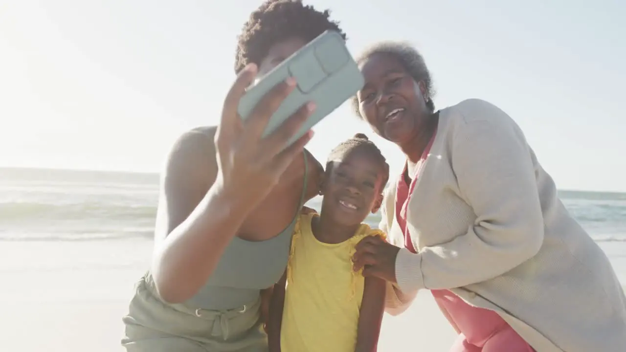 Happy african american grandmother mother and daughter taking selfie at beach in slow motion