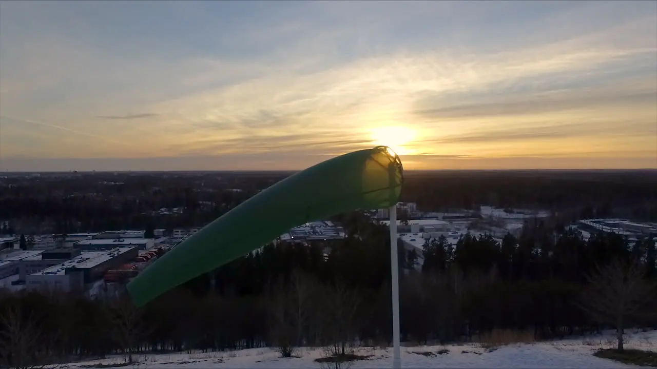 Close up aerial shot of a windsock billowing in a steady breeze on a crisp early morning with the sun slowly rising in the background