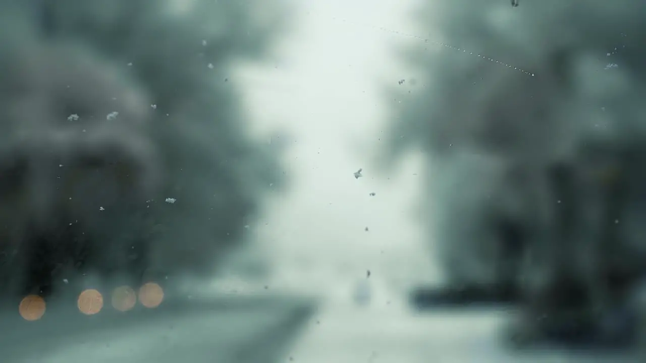 Inside view of the front windshield of a car with wet snow falling onto it and windshield wipers cleaning it off