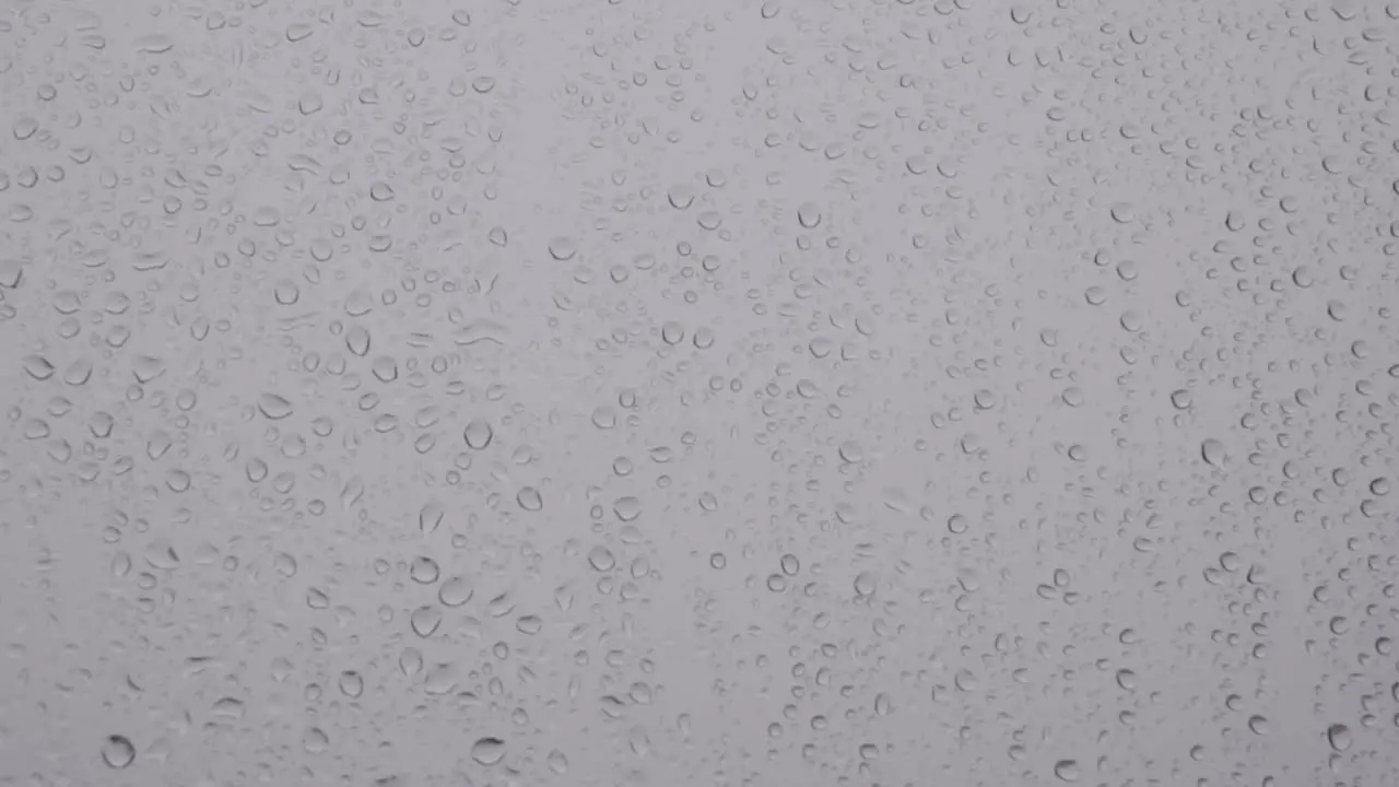 Droplets of rain slowly roll down window pane Static Closeup Background