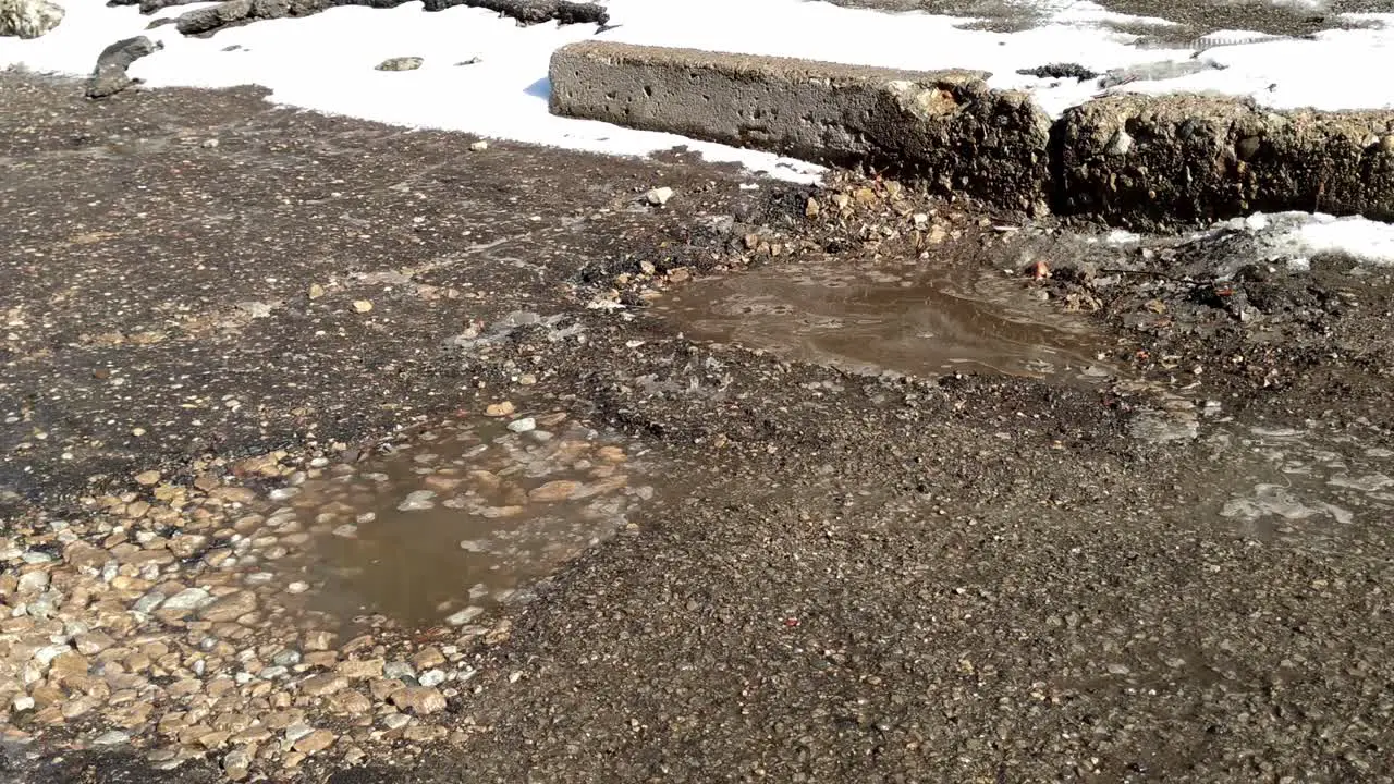 Moving along a broken road with snow on the edges and potholes filled with water and rocks