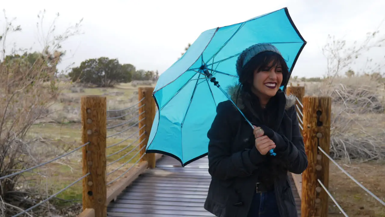 A pretty woman walking in rain and windy bad weather during a storm with a blue umbrella as she smiles and laughs