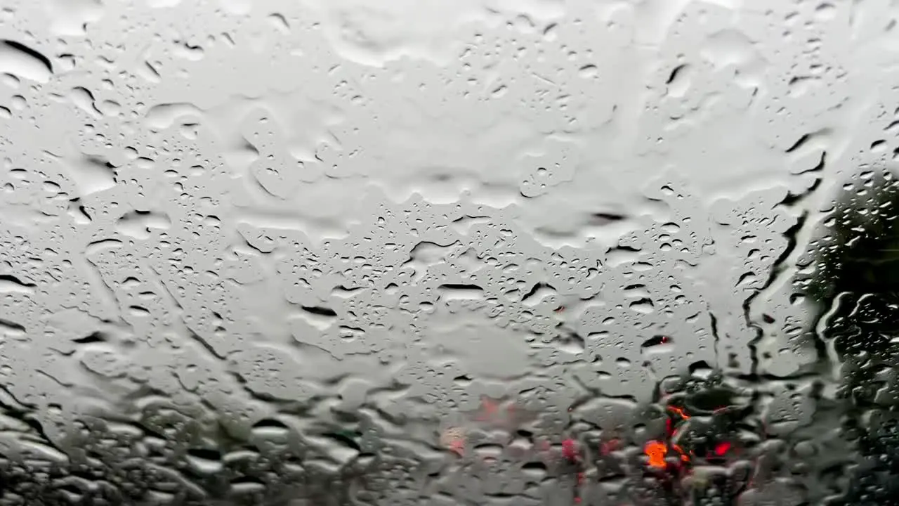 Raindrops on windscreen and red blurred lights of car traffic in background wiper cleaning windshield from pouring rain