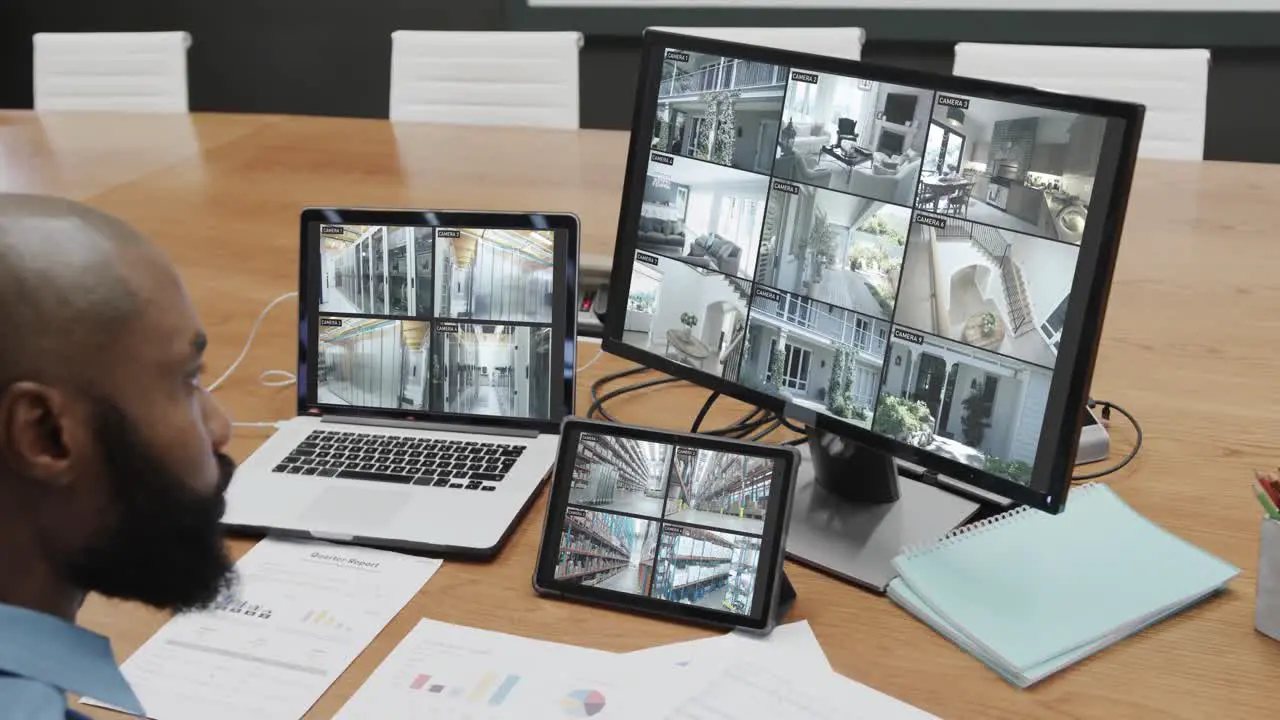 African american male security officer watching cctv camera views on three screens slow motion