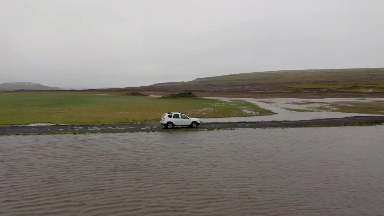 Aerial Side follow of white car passing through a shallow river