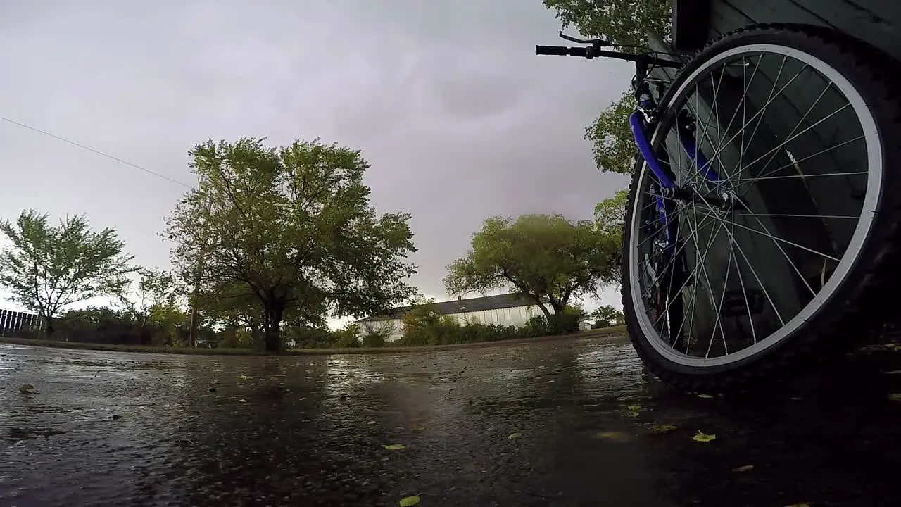 Bike leaning up against a blue wooden fence in the driveway of a house on a rainy day