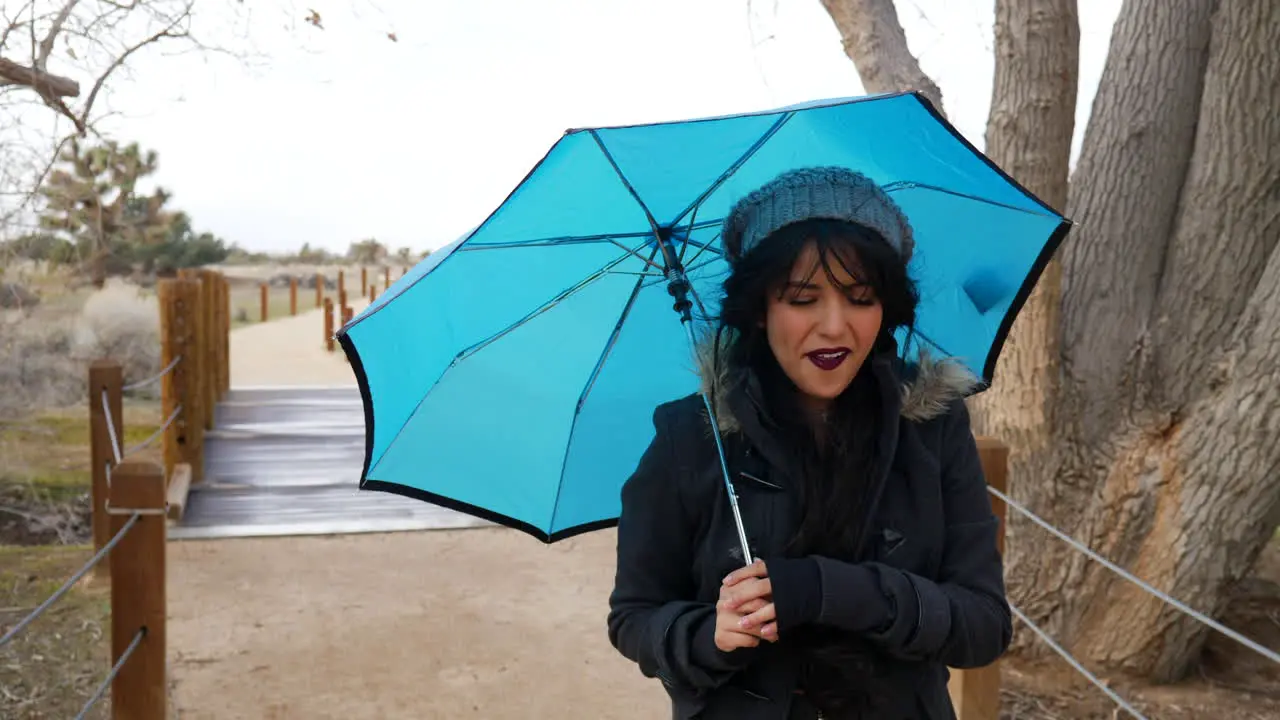 A cute woman smiling and walking in a rain storm with a blue umbrella to protect her from the strong winds and bad weather SLOW MOTION