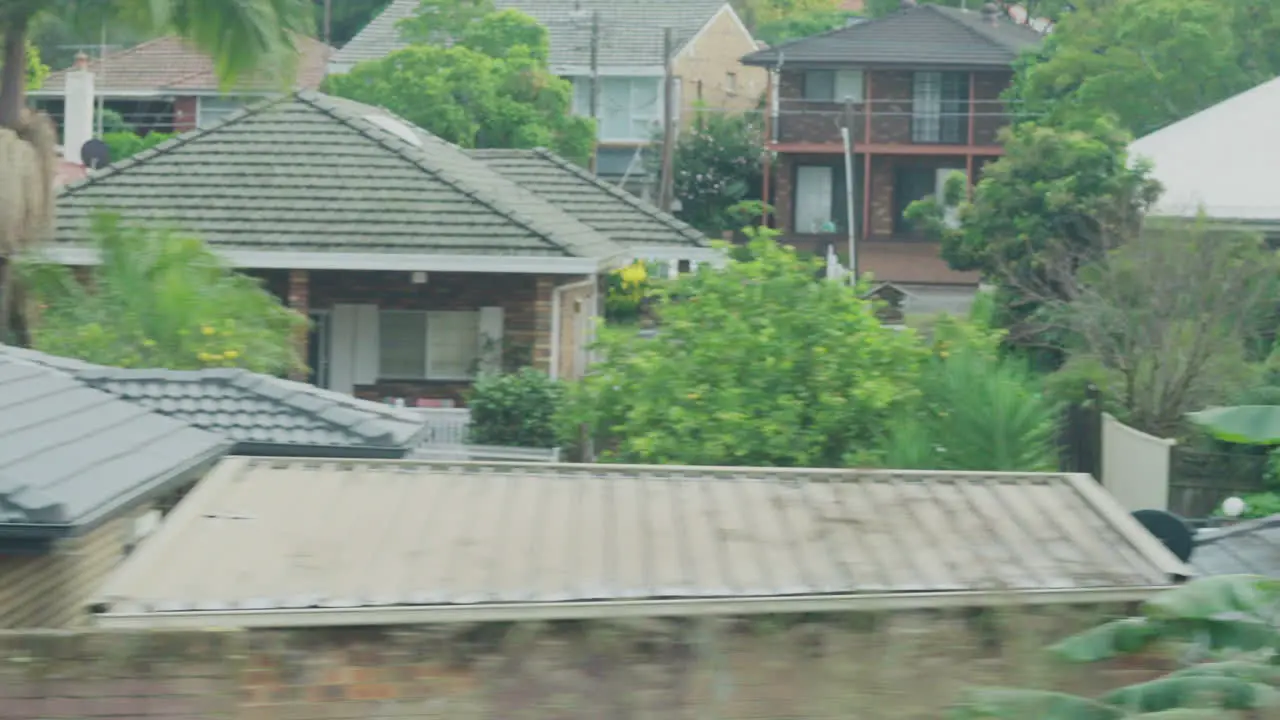 Filming out of a train window during the early dawn passing buildings and backyards in Sydney Australia