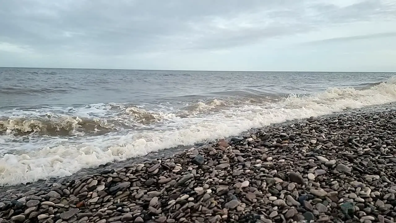 Sandy ocean waves crashing slow motion on Welsh pebble beach in windy autumn season