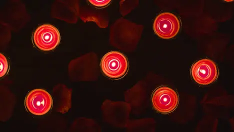 Overhead Shot Of Romantic Lit Red Candles Revolving On Background Covered In Rose Petals 2