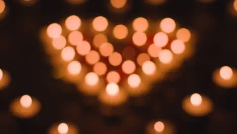 Defocused Shot Of Romantic Red And White Candles In the Shape Of A Heart On Black Background