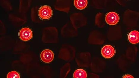 Overhead Shot Of Romantic Lit Red Candles Revolving On Background Covered In Rose Petals With Copy Space