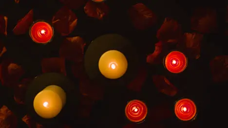 Overhead Shot Of Romantic Lit Red Candles Revolving On Background Covered In Rose Petals