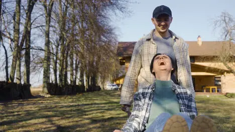 Front view of caucasian man carrying his partner on a wheelbarrow in the countryside Their dog walks around them