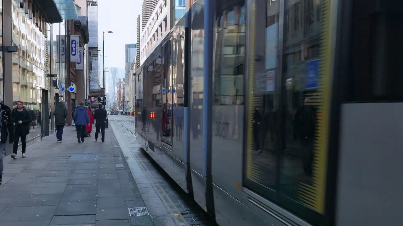 People walking down a street in Manchester with a tram going down