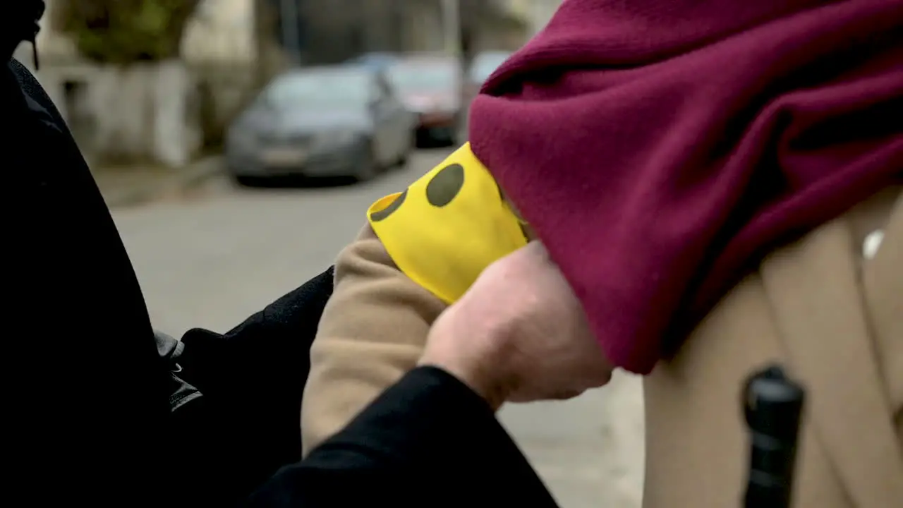 Man Putting An Yellow Armband With Three Black Points On A Blind Woman In The Street