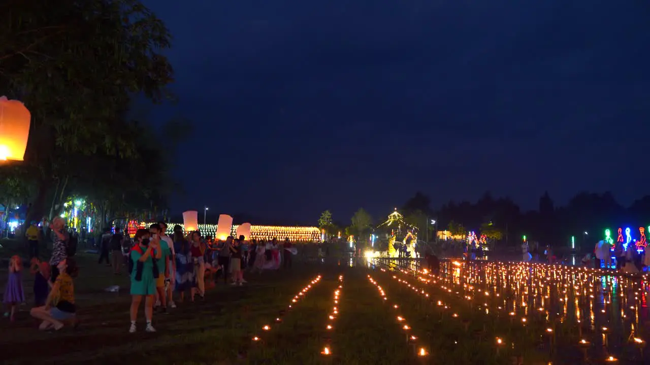 People lighting up floating lanterns at lake with candle lights during Yi Peng