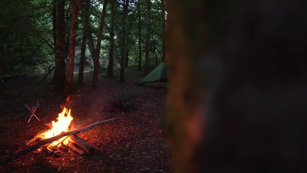 Two tents at night in the woods with campfire burning revealing dolly slider shot