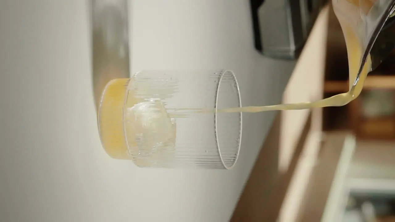 Vertical Video pouring fresh pressed orange juice into drinking glass in the kitchen slow motion close up