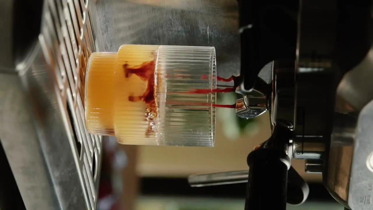 Vertical Video Making orange espresso at home extracting espresso from a portafilter into drinking glass slow motion close up