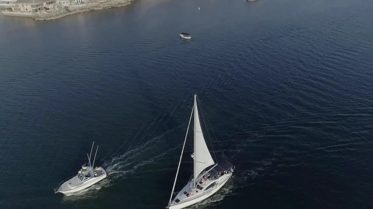 Aerial shot of a white sailboat and a fishing boat heading into the Newport Bay in Newport Beach California with Pirates Cove in the background