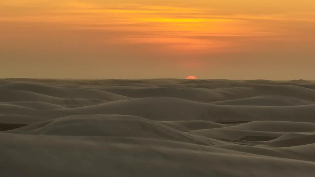 Vibrant orange sunset over undulating sand dune landscape aerial left