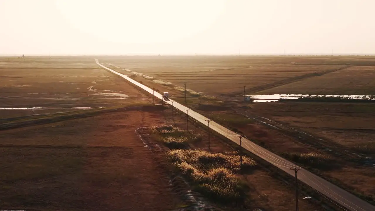 Aerial tracking shot of a transport truck that navigates a straight road forging ahead towards the radiant embrace of the setting sun 4K60FPS cinematic grade