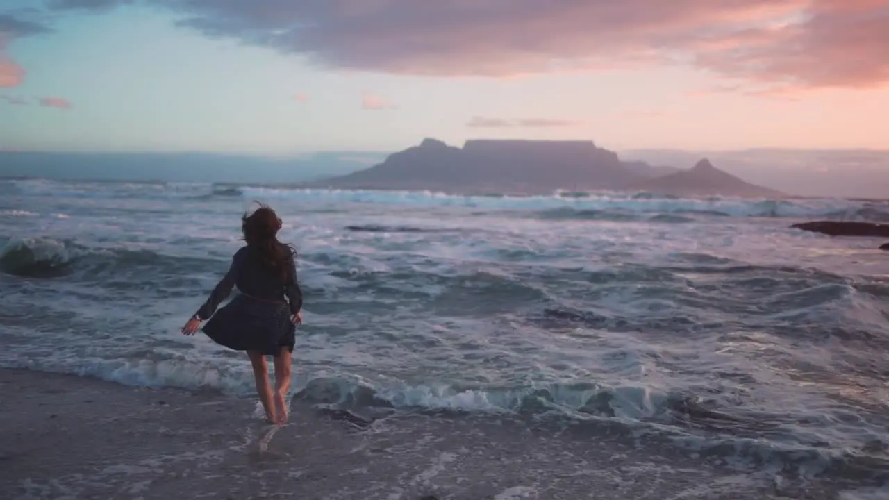 slow motion video of a woman running into the sea and dancing in the extremely wavy water just as the sun goes down while camping on the beach