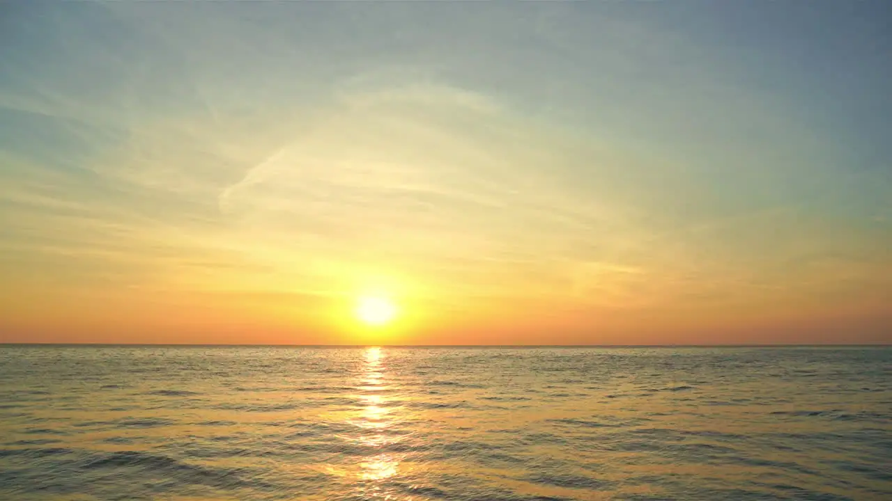 A huge yellow sun on the ocean horizon the sunset sky is pink orange yellow and blue