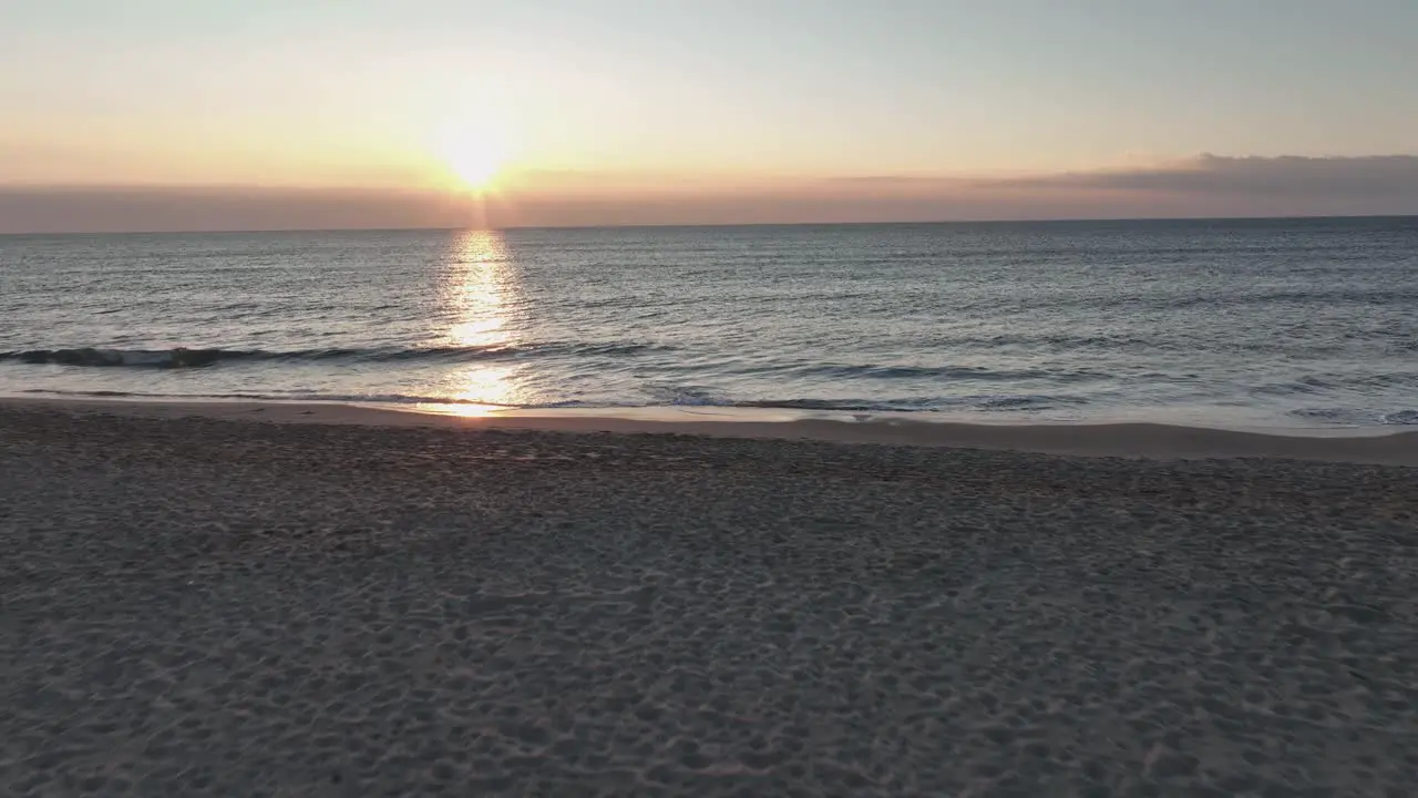 A mesmerising sunset on a beach flying over a beach and steadily following the sun that is reflecting on the water surface