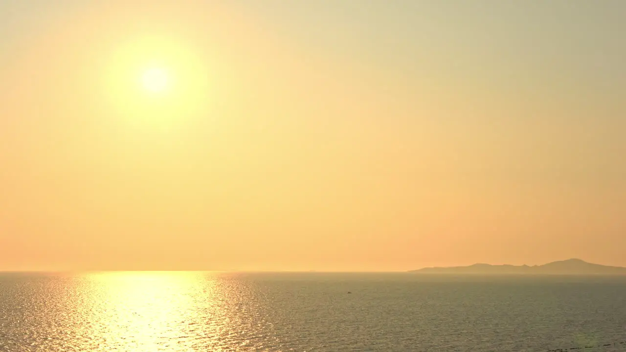 A golden sun hangs over a golden ocean and island mountains