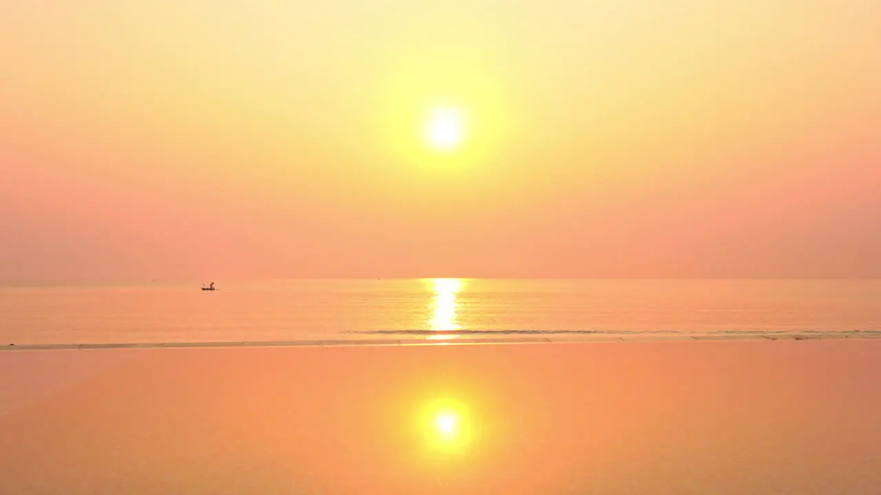 A lone boat drifts under a dramatic colorful ocean sunset