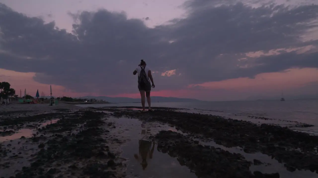 Wide low angle shot of caucasian woman walking on a beach late evening with beautiful sunset in the background 4K