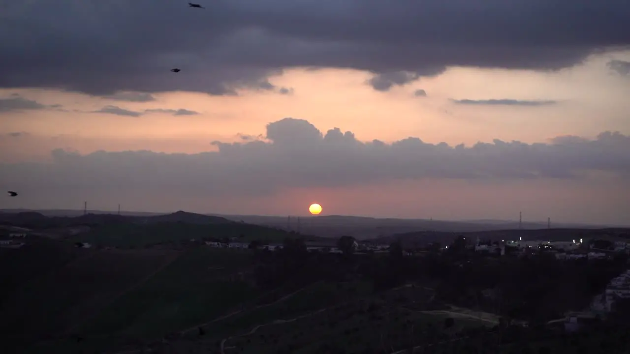 Silhouetted sky with setting sun and birds flying in slow motion