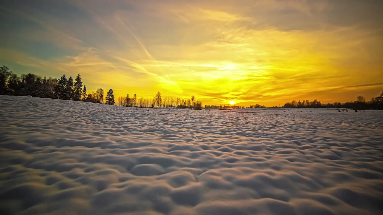 Dramatic golden sunset time lapse sun dips behind the horizon beyond a field of snow and trees