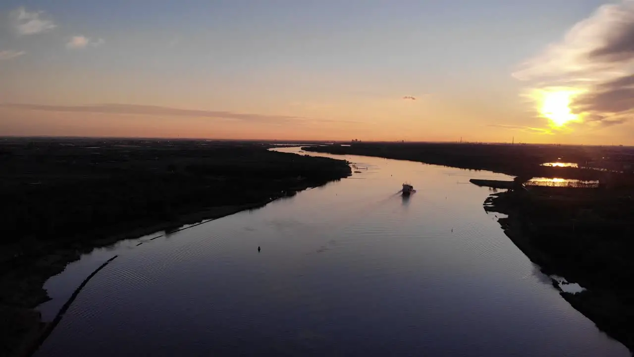 Ariel pull back shot by drone of a shipping vessel carrying container travelling through water channel during dusk