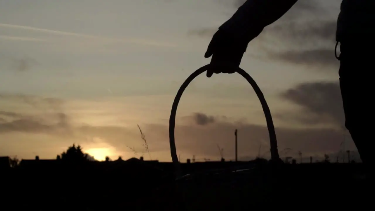 Silhouette of woman carrying woven basket in countryside at sunset