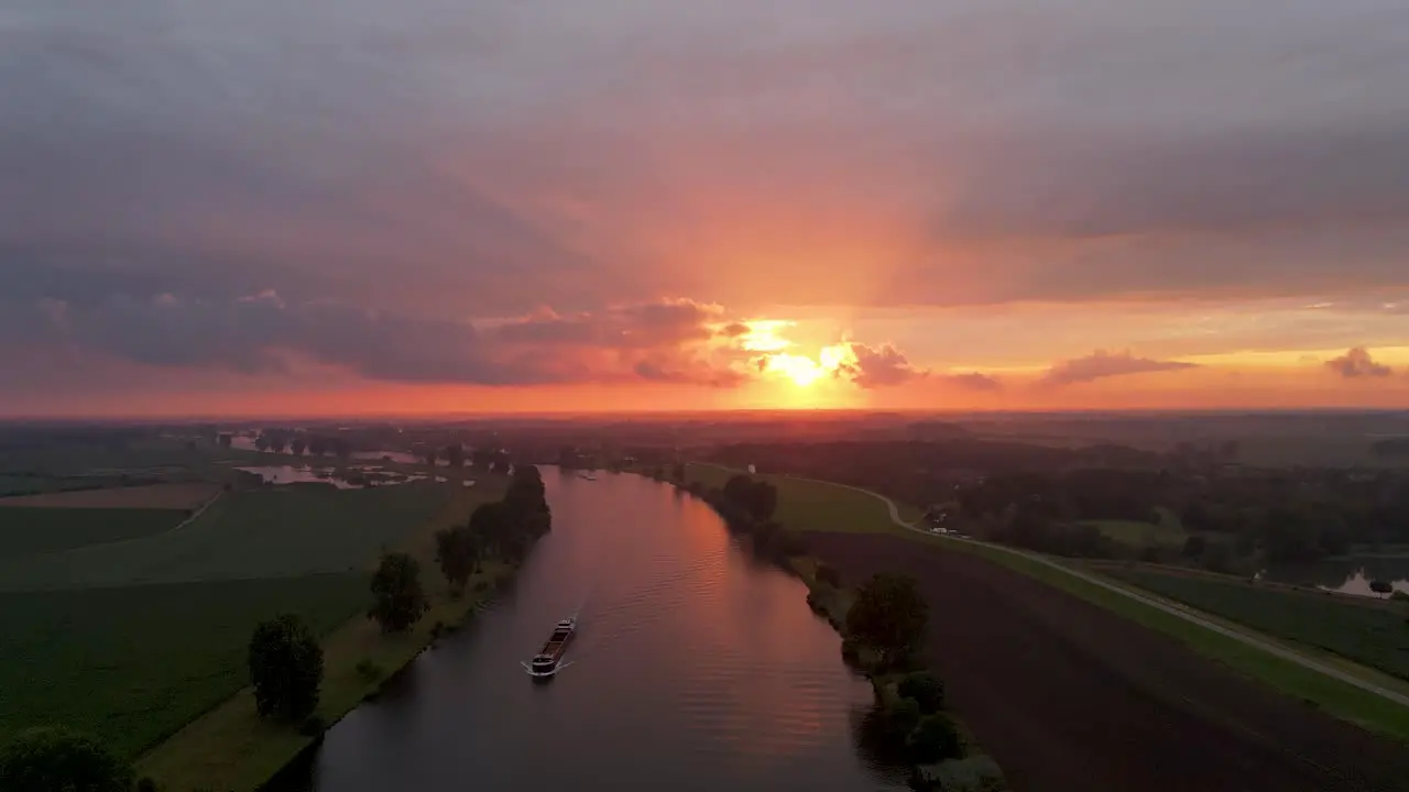 An aerial shot of a Beautiful sunset over Dutch river where a vessel passes by in an orange and red scenery