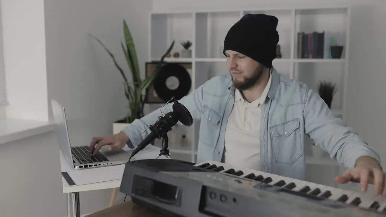 Male Musician Playing Electric Keyboard And Using A Laptop At Home