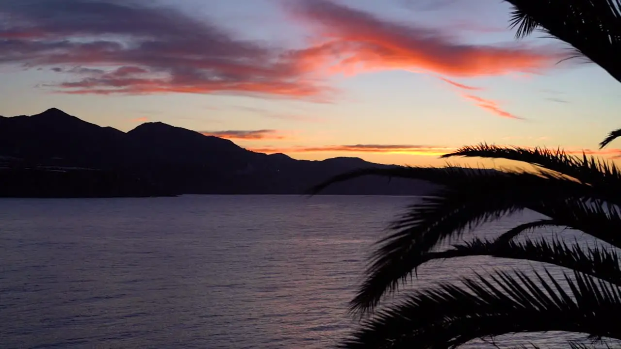 Beautiful sunset over ocean with palm leafs and mountain silhouette